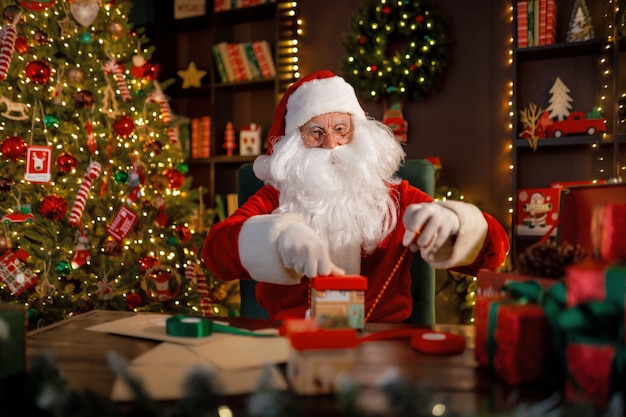 Santa clause is preparing gifts for children for xmas while sitting at his desk at home new year