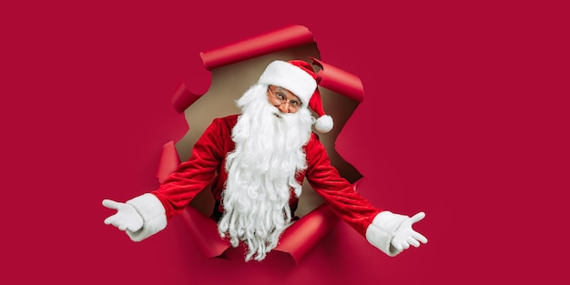 Santa Clause looking through hole on red paper while gesturing hands like welcome New Year advert