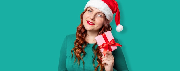 Santa hat smile woman with christmas gift box on green wall new year celebration banner copy space w...