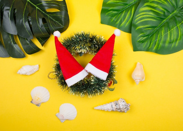 Santa hats on a Christmas wreath, tropical leaves and seashells