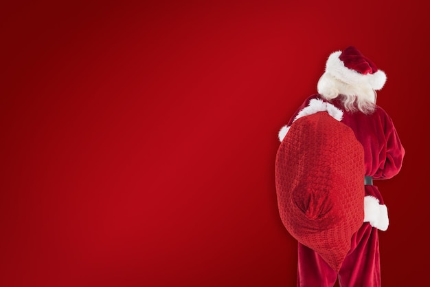 Santa is holding his bag in one hand against red background