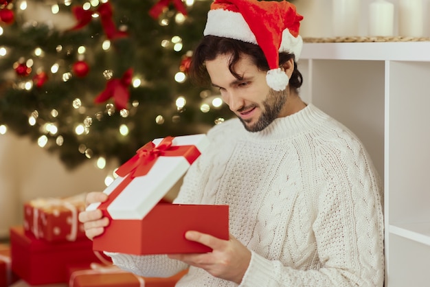 Santa man with present in the gift box near christmas tree at home