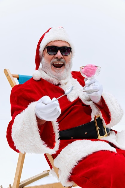 Photo santa takes bite of ice cream from glass bowl smiling widely in his sunglasses clearly enjoying his