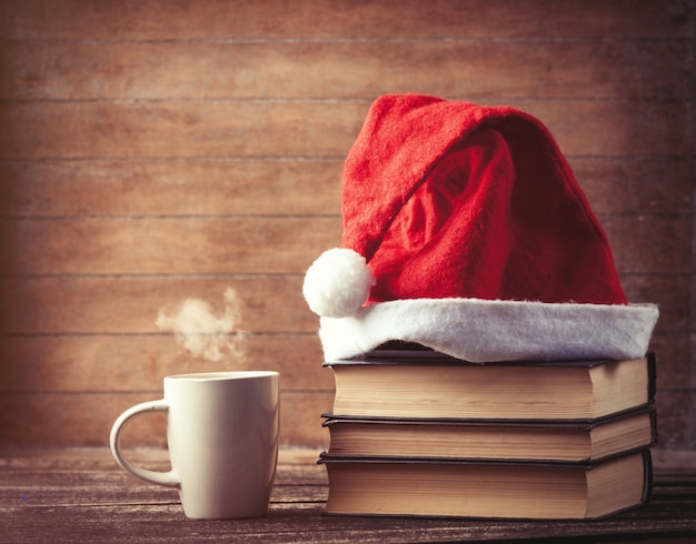 Santas hat over books near hot cup of coffee or tea 