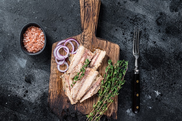 Sardine fish fillet in olive oil on wooden board. Black background. Top view.