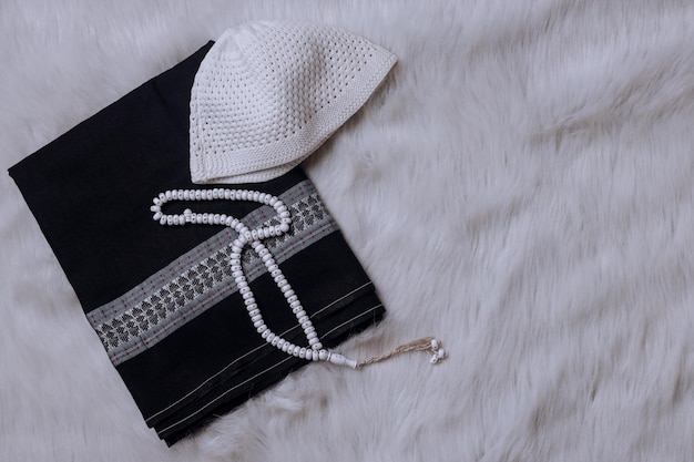 Sarong, skull cap and prayer beads on white soft rug, islamic background with copy space.