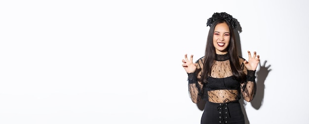 Sassy beautiful asian woman in black lace dress and wreath trying to scare you raising hands up acti