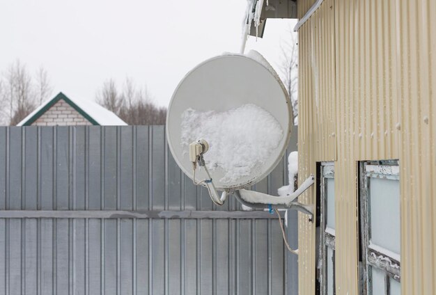 Satellite dish fixed to the wall of a house in the snow after a snowfall