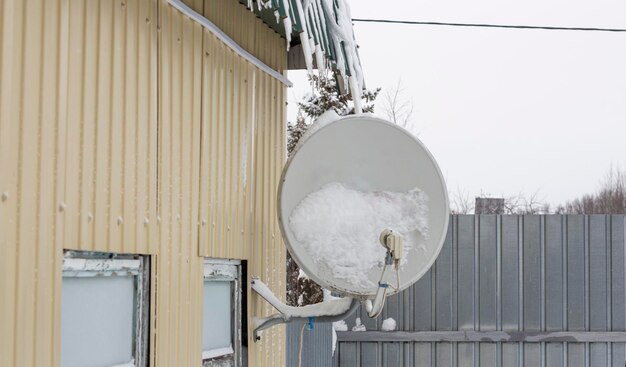 Satellite dish fixed to the wall of a house in the snow after a snowfall