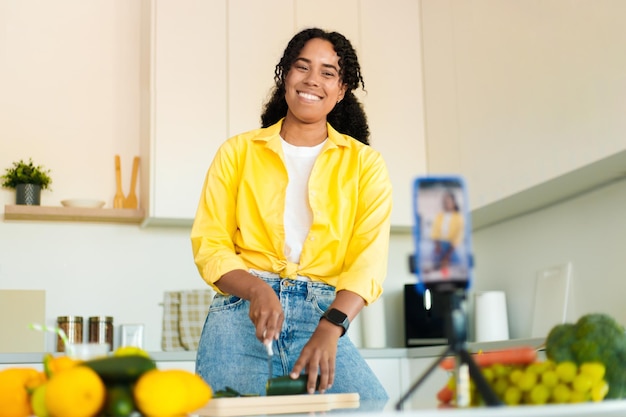 Satisfied african american woman cooking and recording video lesson on smartphone in kitchen interior