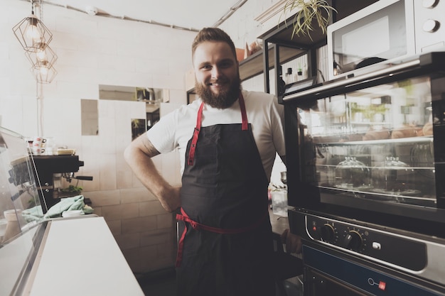 Satisfied bearded baker apron stands next to oven