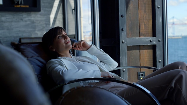 Satisfied businesswoman watching sea view big window Boss laying at armchair