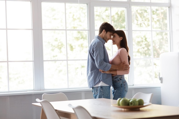 Satisfied cheerful young husband and wife dancing and hugging together in kitchen interior