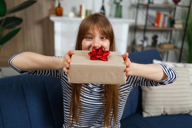 Satisfied girl looks with admiration at a gift box while sitting on the couch indoor