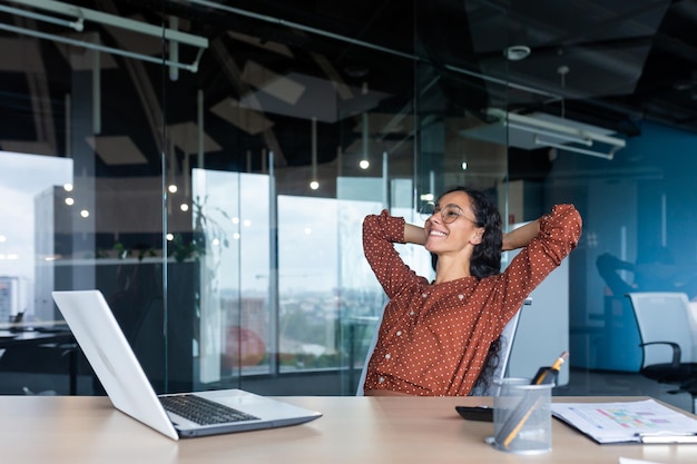 Satisfied happy and successful business woman smiling and resting hispanic female worker finished