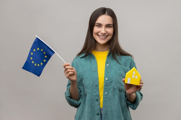 Satisfied holding european flag and paper house dreaming to buy accommodation in Europe