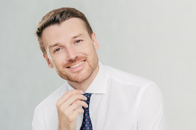 Satisfied male worker with positive expression has broad smile rejoices sucessful agreement with partner wears elegant clothes isolated over white studio wall People positive emotions concept