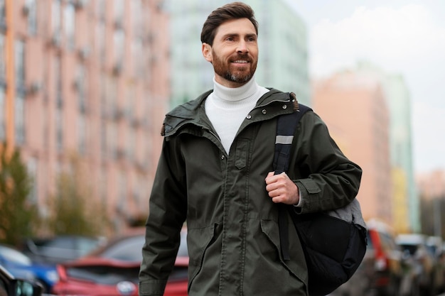 Satisfied pleasant man in outerwear with a backpack walks outdoors