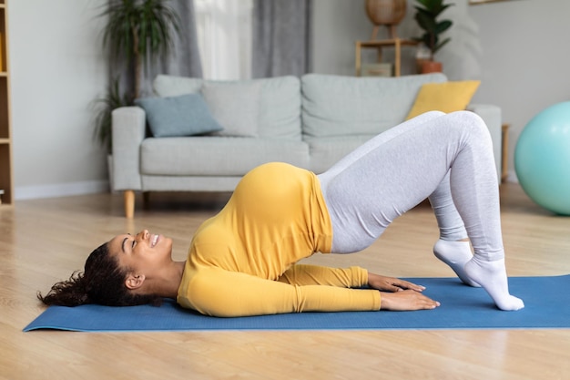 Satisfied young black pregnant woman with big belly practicing yoga on mat enjoy workout