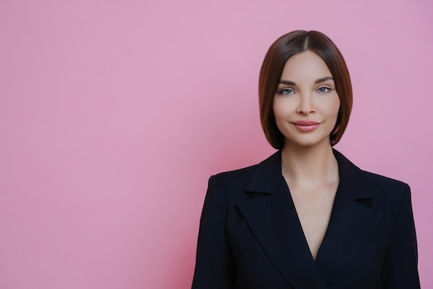 Satisfied young woman in formal attire calm expression posing against pink background copy space for ads