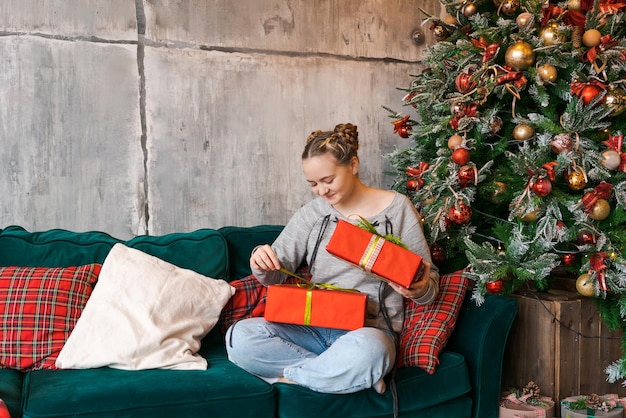 Satisfied young woman holding Christmas gifts next to festive tree Festive New