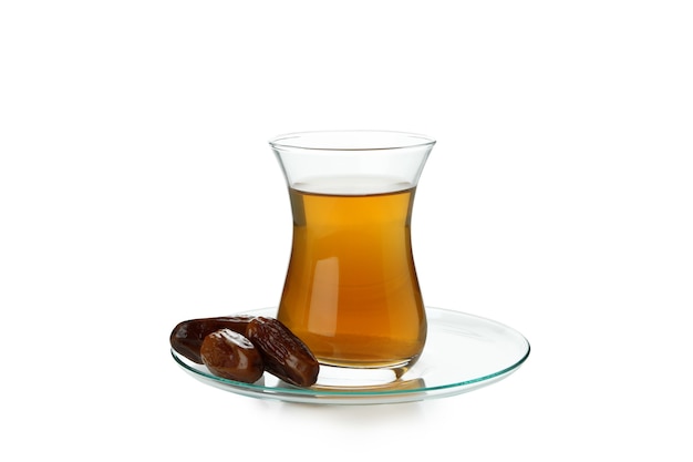 Saucer with glass of tea and dates isolated on white surface