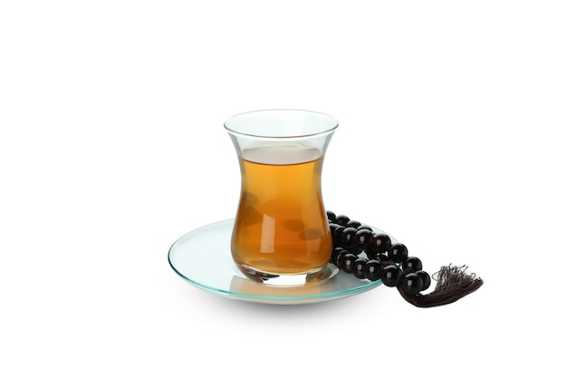 Saucer with glass of tea and rosary isolated on white