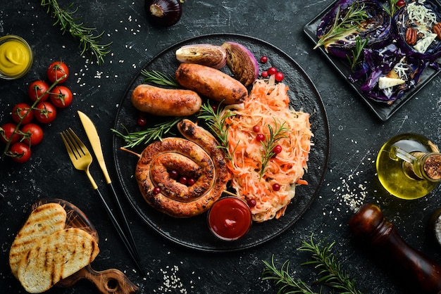 Sauerkraut and grilled sausages with rosemary and cranberries on a black plate Traditional German dish Top view On a black stone background