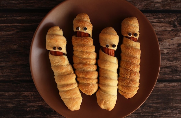 Sausage in the dough in the form of a mummy on a brown plate for the Halloween holiday