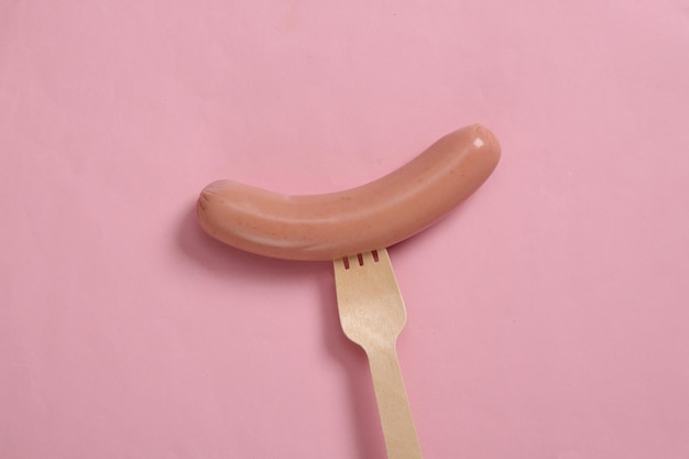 Sausage on a wooden fork Minimalism food and eco concept Pink background