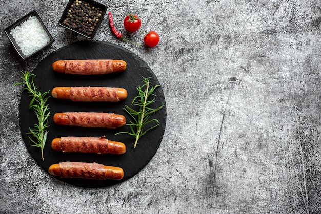 Sausages on a black plate with a bowl of spices and tomatoes.