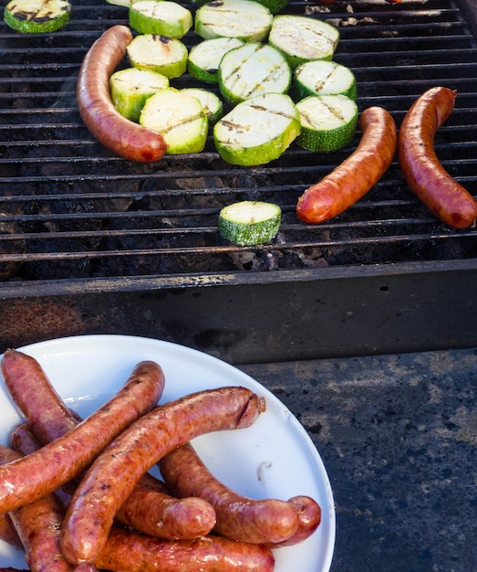 Sausages and fresh vegetables zucchini grilling on a barbecue outdoors