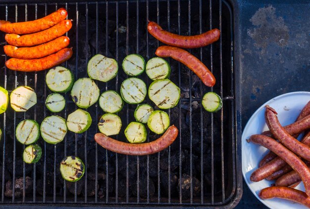 Sausages and fresh vegetables zucchini grilling on a barbecue outdoors