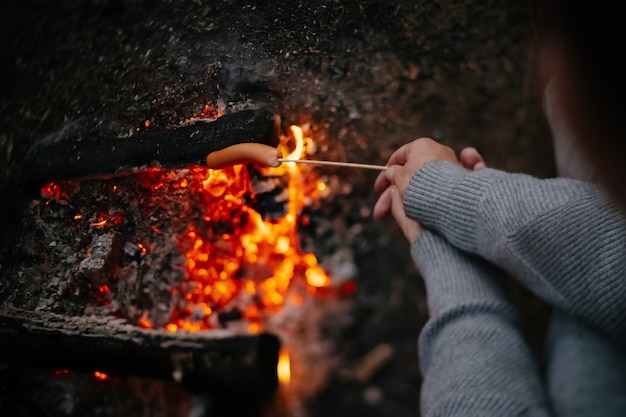 Sausages fried on a fire on a wooden rod in a summer forest concept of tourism and camping