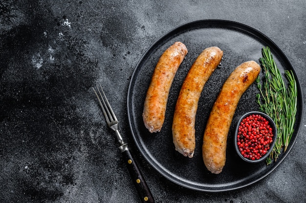 Sausages fried with spices and herbs on a plate. Top view. Black background. Copy space.