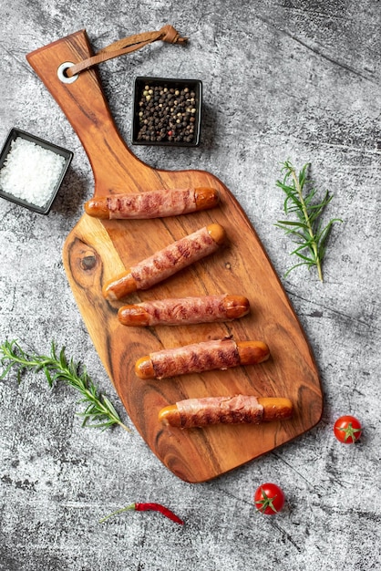 Sausages on a wooden board with a bowl of herbs and a small bowl of salt.