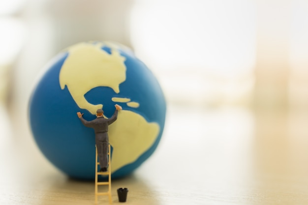 Save Global Environment Care Concept. Close up of worker miniature people standing on stair and cleaning mini world ball with water tank on wooden table 