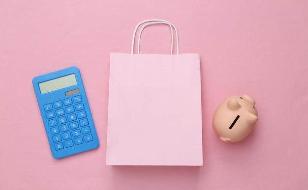 Save money Sale concept Shopping bag with calculator piggy bank on pink background Top view