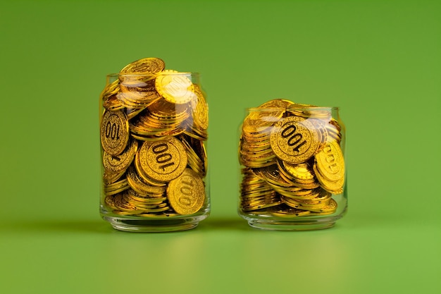 Saving gold coins in glass jars on green background coin savings concept