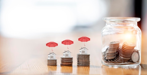 Savings Insurance and Investments concept House model on the stack of coins and coin in glass jar on wooden tabel