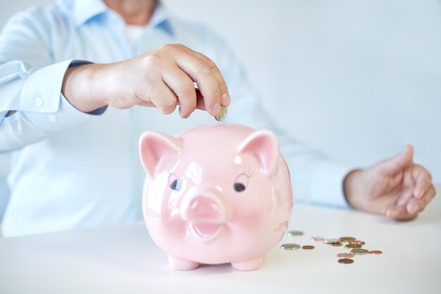 savings, oldness, business, people and banking concept - close up of senior man hands putting coins into piggy bank