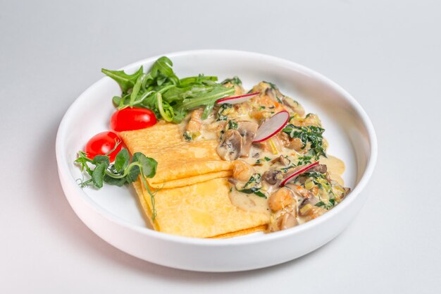 Savory crepe with creamy mushroom sauce and fresh greens on a white plate