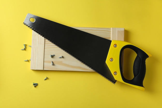 Saw, screws and wooden board on yellow background