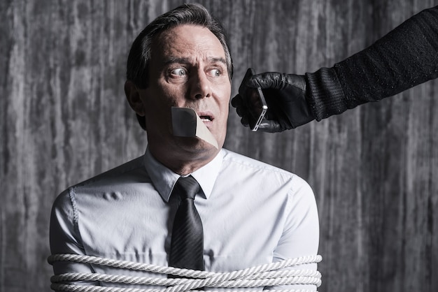 Photo say a few words to your nearest! tied up businessman sitting in front of the dirty wall while someone stretching out hand with mobile phone