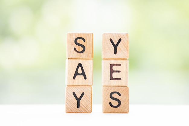 SAY YES word is written on wooden cubes on a green summer background Closeup of wooden elements