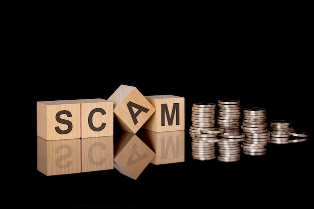 SCAM text on wooden cubes on dark backround with coins business concept