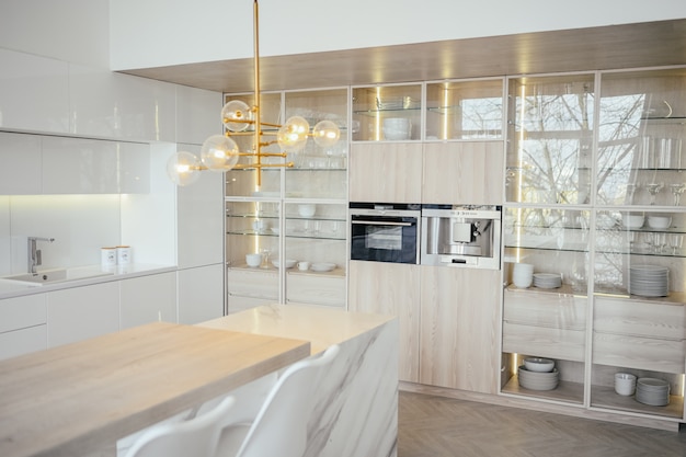 Scandinavian empty classic modern luxury kitchen with wooden, white, marble details, new stylish furniture, minimalistic nordic interior design. Bar stools, glass display rack, dishes and glassware