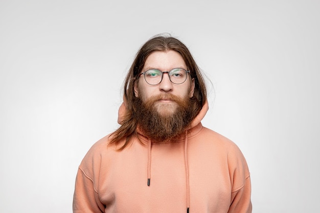 Scandinavian handsome serious man with glasses and face hair isolated on gray background in orange sweatshirt Calm nordic guy with long ginger hair and beard