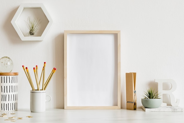 Scandinavian home office interior with wooden mock up poster frame, design office accessories, tapes, supplies, notes, memo sticks, air plants. Minimalistic concept. Template.