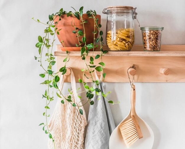 Photo scandinavian kitchen interior wooden shelfhanger on a gray wall with a flower a jar of dry pasta granola and linen towels eco style interior